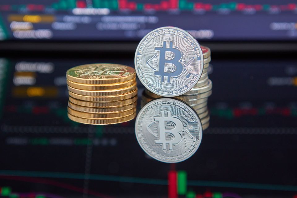 Moedas de Bitcoin empilhadas diante de um gráfico de negociação exibindo tendências do mercado de criptomoedas.