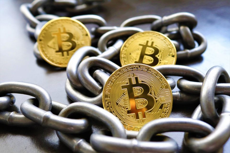Moedas de Bitcoin entrelaçadas por correntes metálicas, simbolizando a segurança e a custódia de criptoativos.